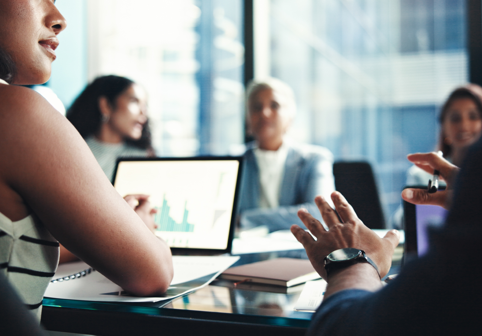Business team in a boardroom discussion, with a laptop showing a bar chart on the table